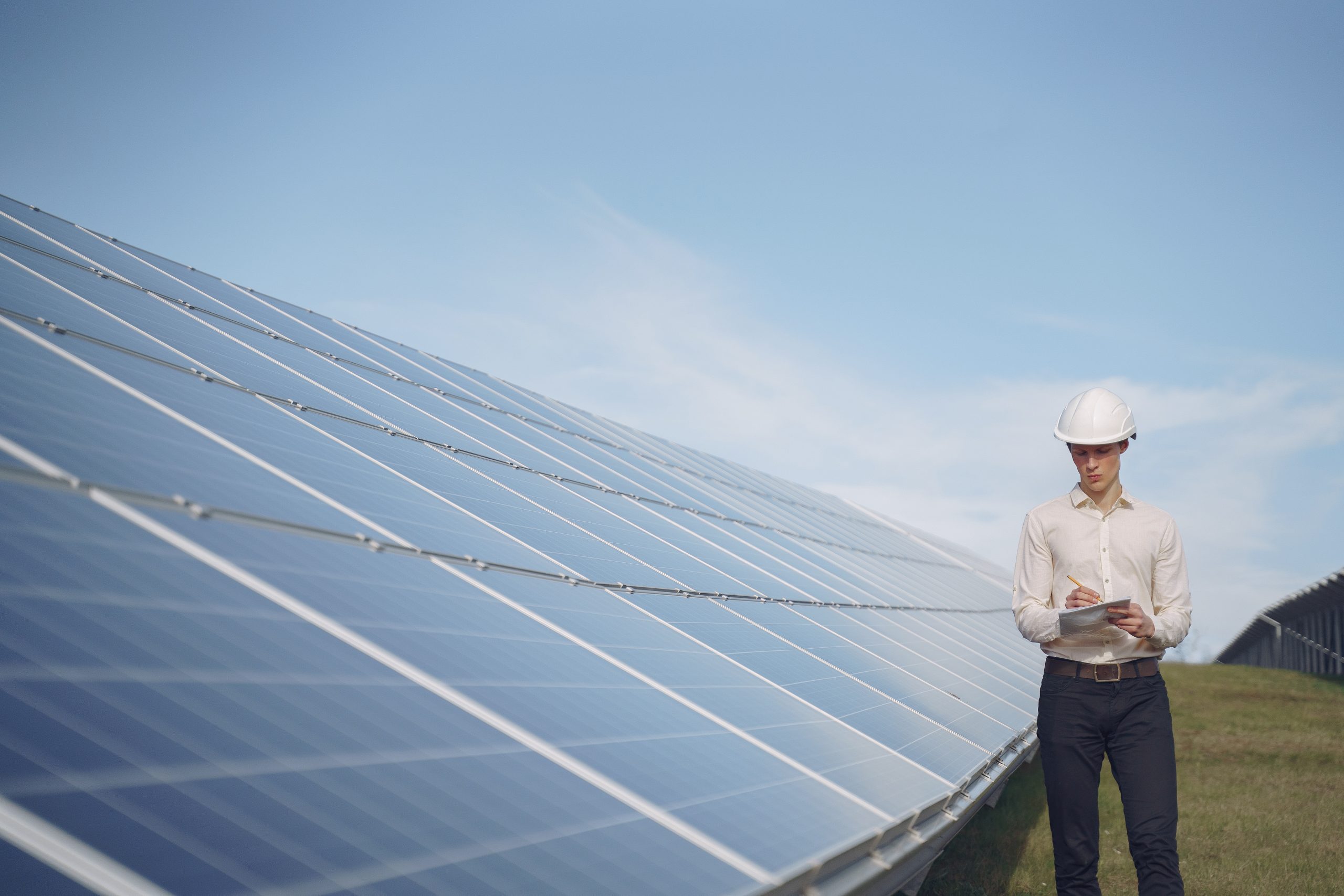 Businessman in a white helmet near solar battery A solar professional examining the performance of solar panels installed at a commercial site. For a free estimate, get in touch today.